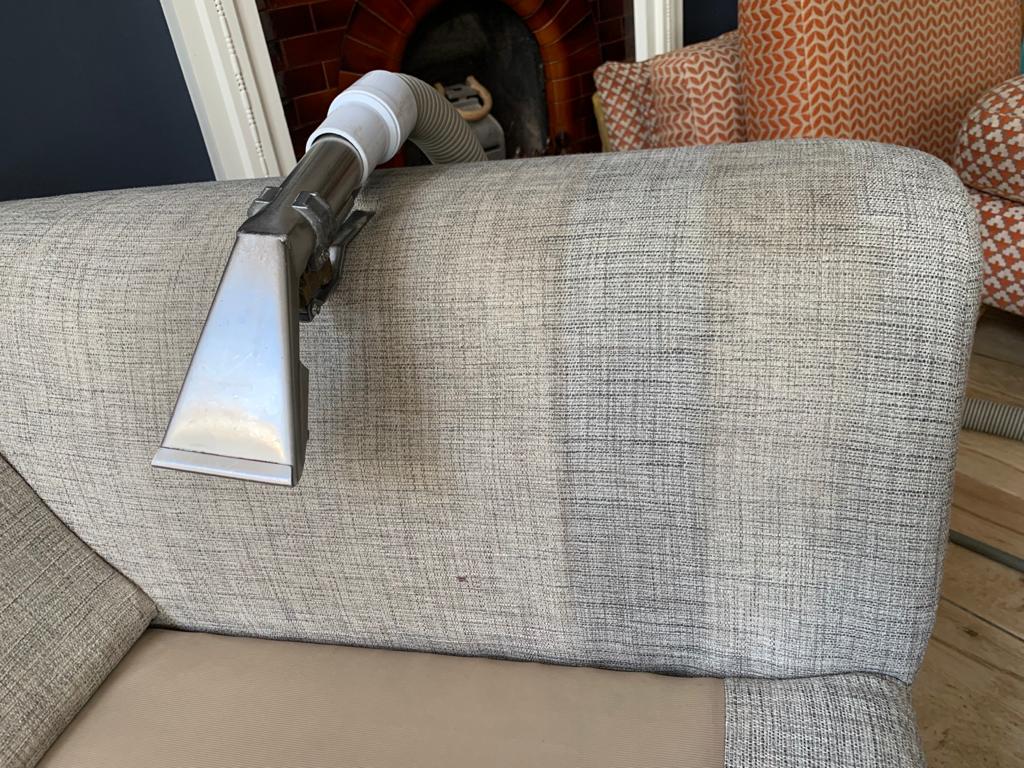 This is a photo of an arm of beige sofa that shows a test patch that has been steam cleaned. The steam cleaning machine is also showing in the photo works carried out by Belsize Park Carpet Cleaning Solutions