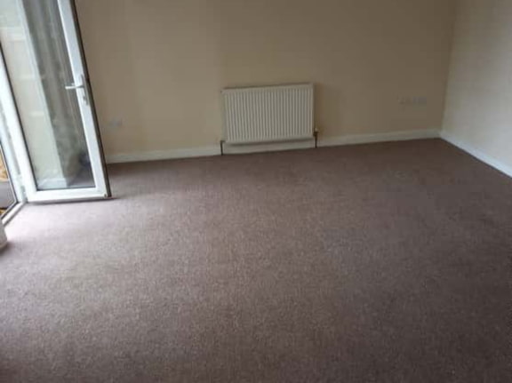 This is a photo of a living room after it has been cleaned. The room is empty and has a brown carpet that has been steam cleaned works carried out by Belsize Park Carpet Cleaning Solutions